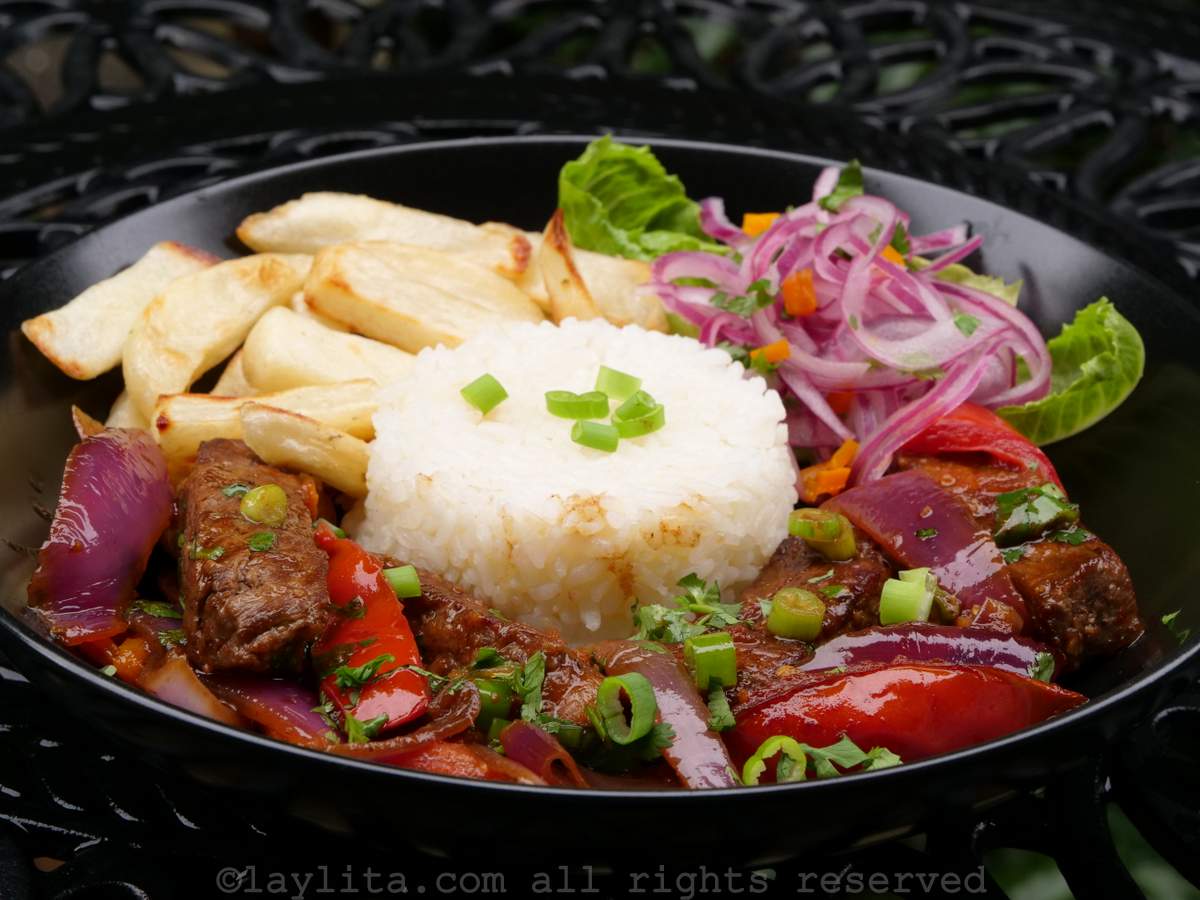 Lomo saltado served on a black plate with rice, French fries, and salad