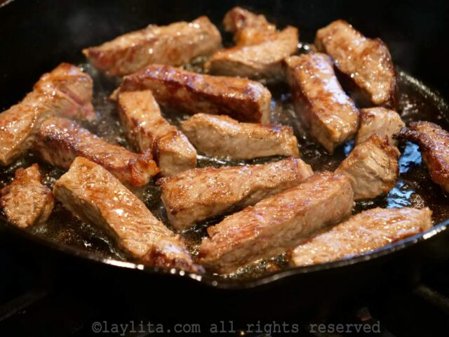 Slices of beef being seared in a pan at high heat