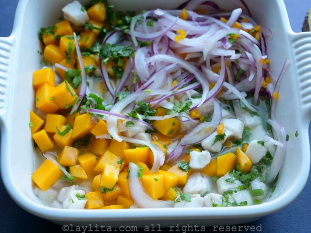 Fish ceviche ingredients in a white dish being mixed. 