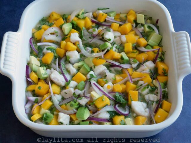 Ceviche with fish, mango and avocado in a white serving dish on a blue backgroun