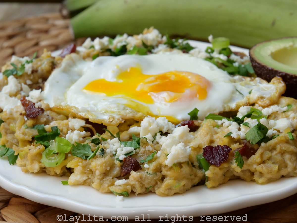 Ecuadorian green plantain tigrillo on a white plate served with a fried egg, cheese and bacon bits