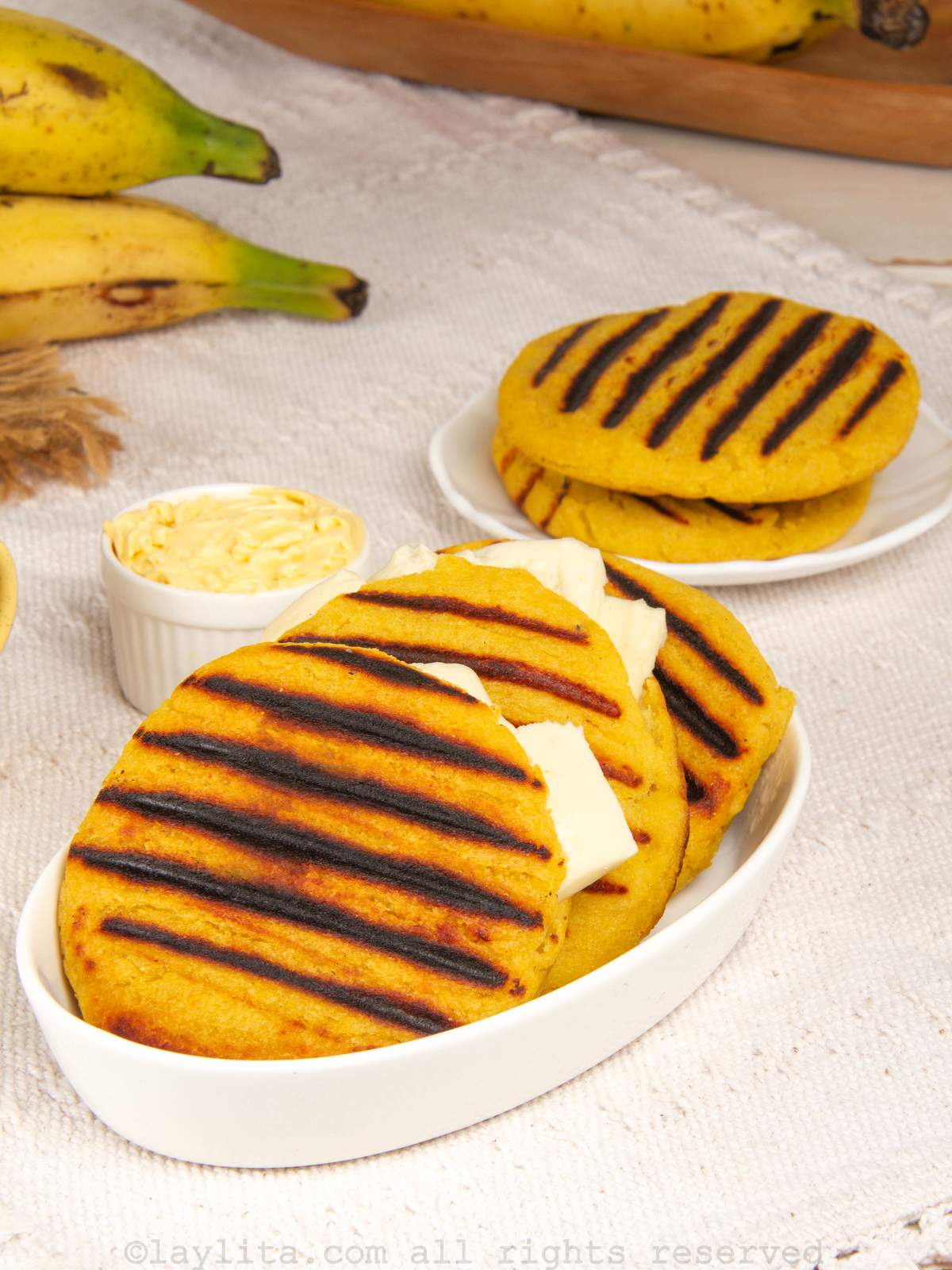 Three ripe plantain arepas grilled and served with cheese in a serving dish.