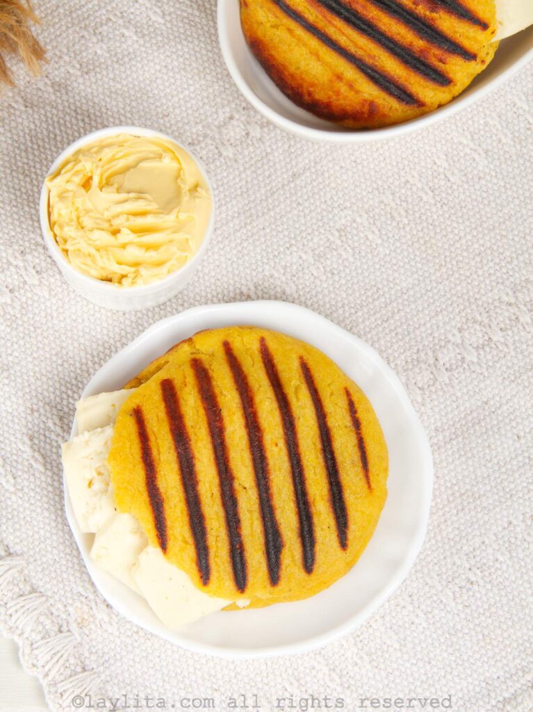 Overhead photo a ripe plantain arepa on a white plate next to a ramekin of butter