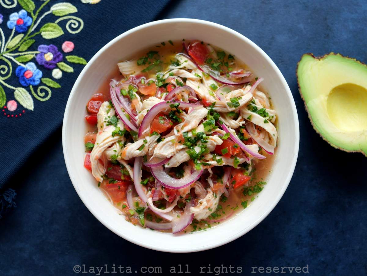 Close up of chicken ceviche in a white bowl with an avocado next to it.