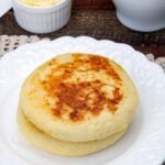 Two arepas stacked on a white plate with a dish of butter next to it