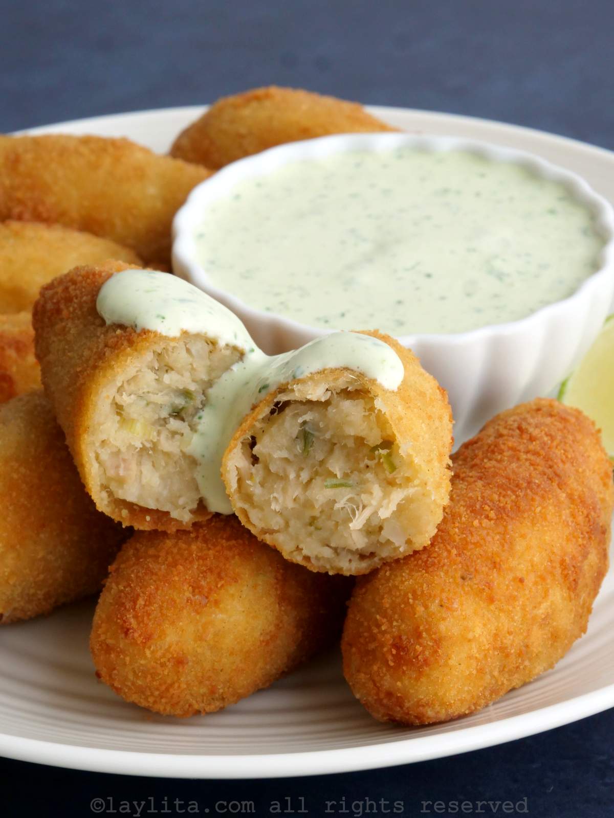 Oval tuna potato croquettes served on a plate with one croquette broken in half and drizzled with sauce.