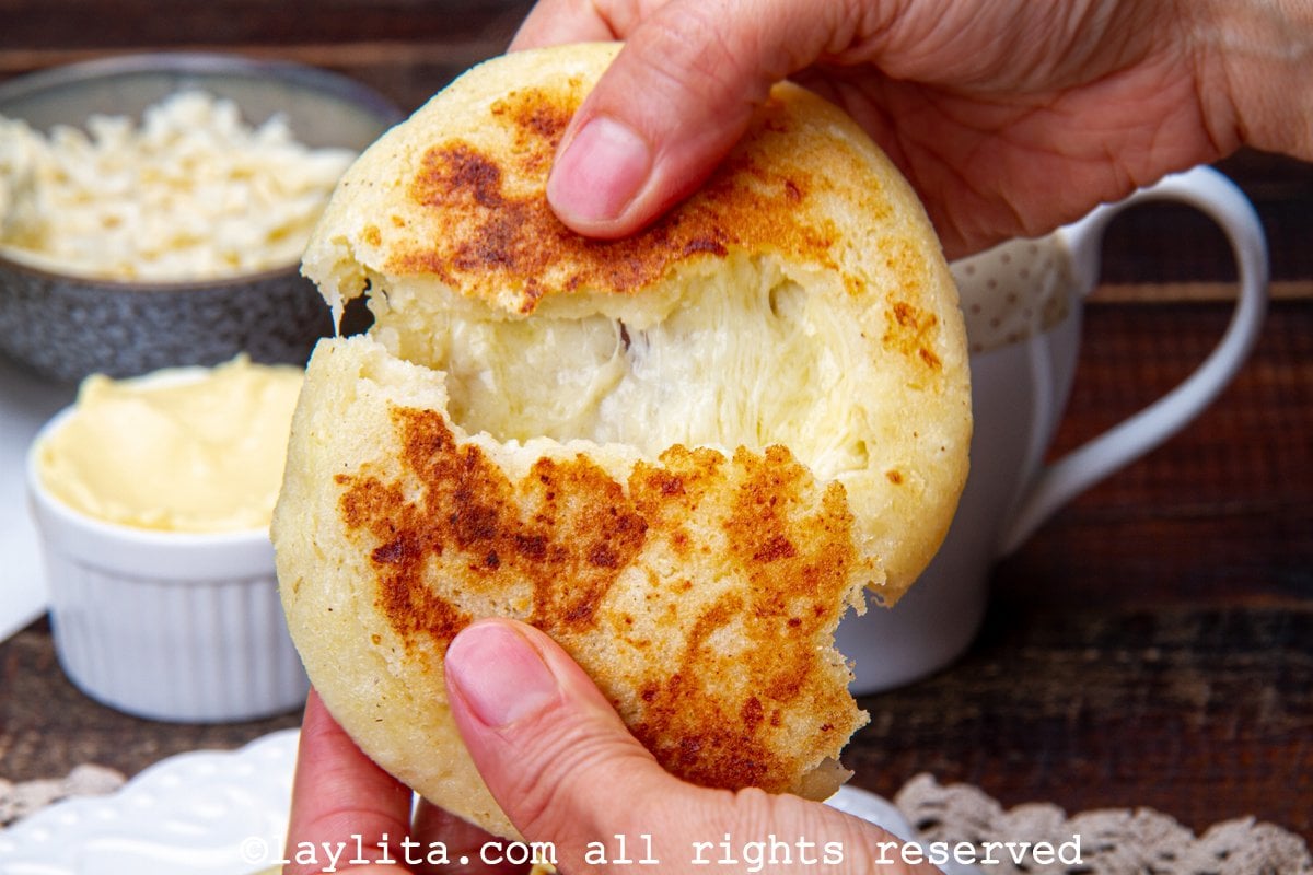 Hands holding a Colombian cheese arepa and pulling it apart to show the melty cheese.