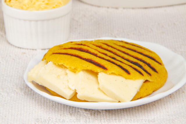 Close up of a ripe plantain arepa on a plate with sliced cheese stuffed in the middle