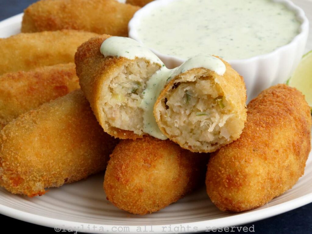 Oval tuna potato croquettes served on a plate with one croquette broken in half and drizzled with sauce.