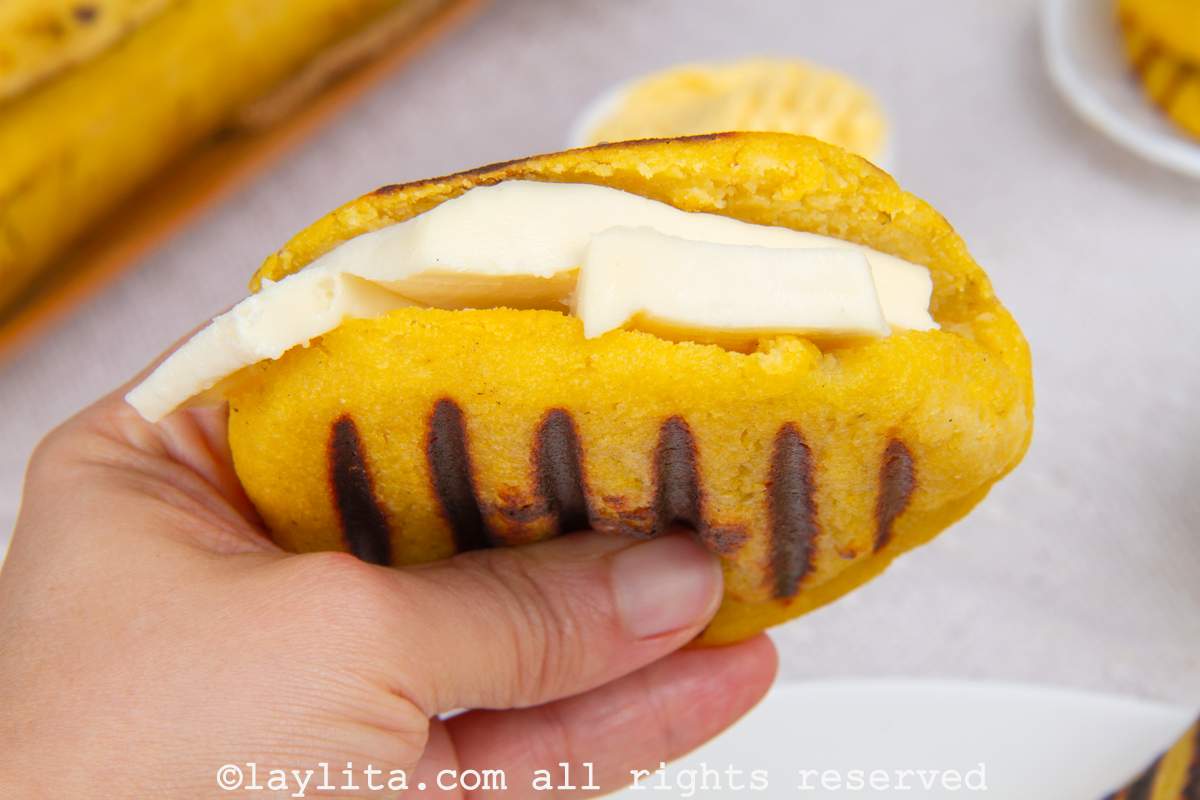 Hand holding a ripe plantain arepa with slices of cheese stuffed inside