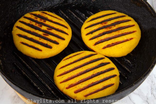 Three ripe plantain arepas cooking on a cast iron skillet