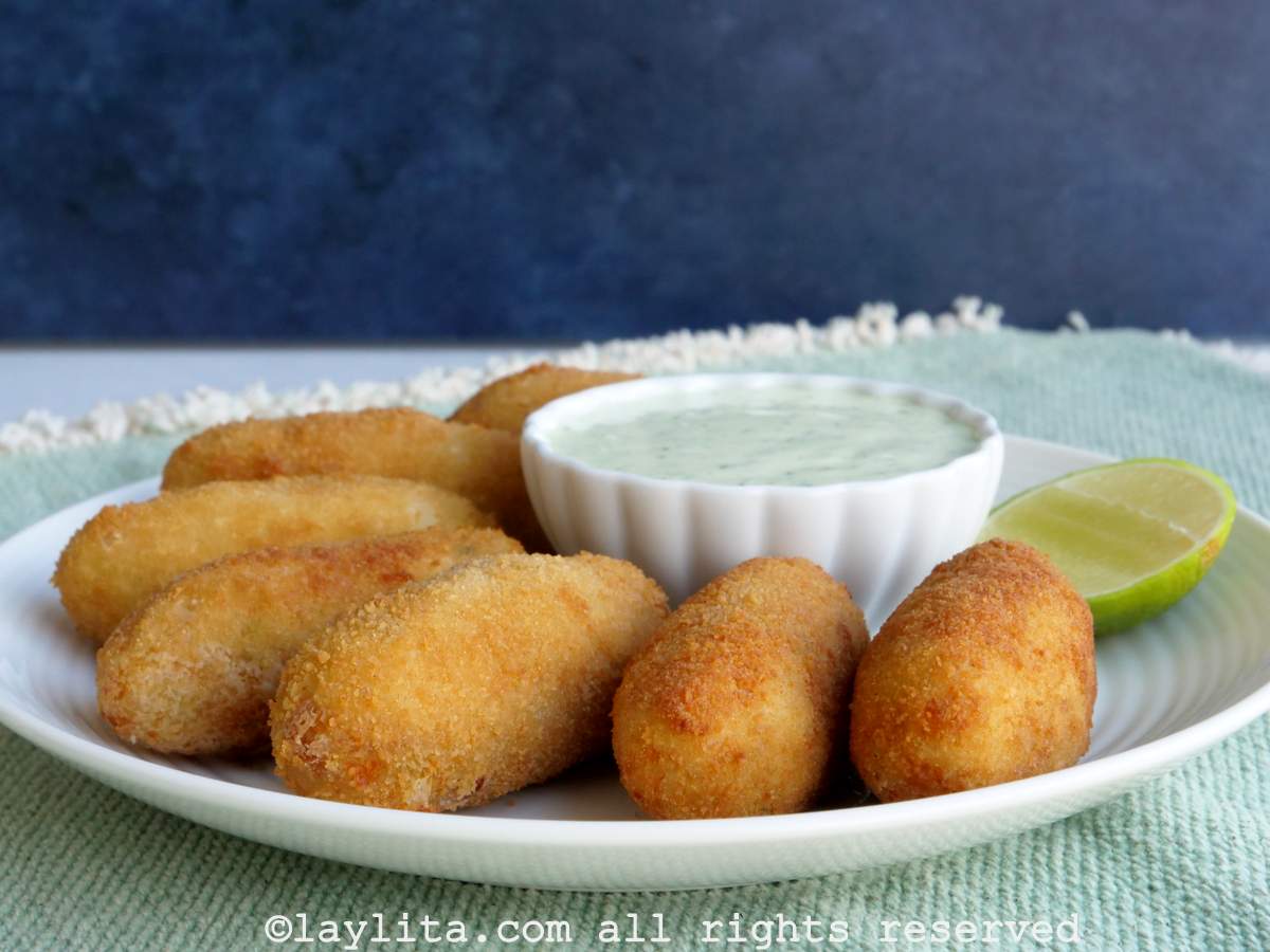 Oval tuna potato croquettes on a plate served with sauce and a lime.