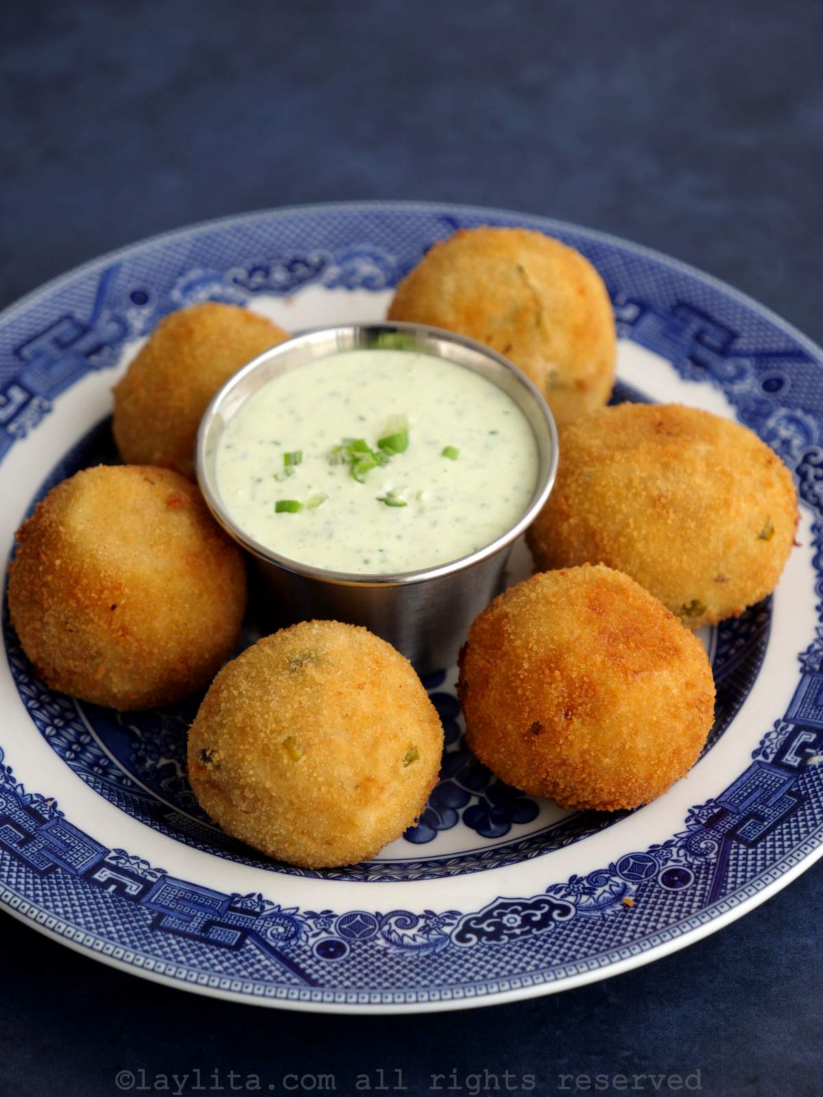 Round tuna potato croquettes on a plate placed around a small ramekin of green sauce.