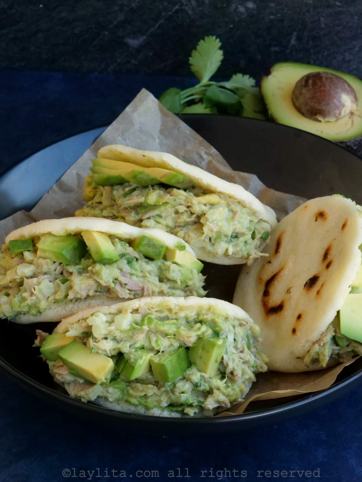 Four tuna avocado stuffed arepas in a bowl with three of them facing the camera to show the filling.