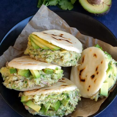Overhead shot of arepas with tuna avocado salad filling served in a bowl lined with parchment paper.
