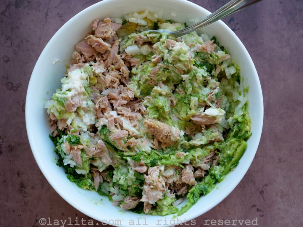 Mixing ingredients for tuna avocado salad in a white bowl