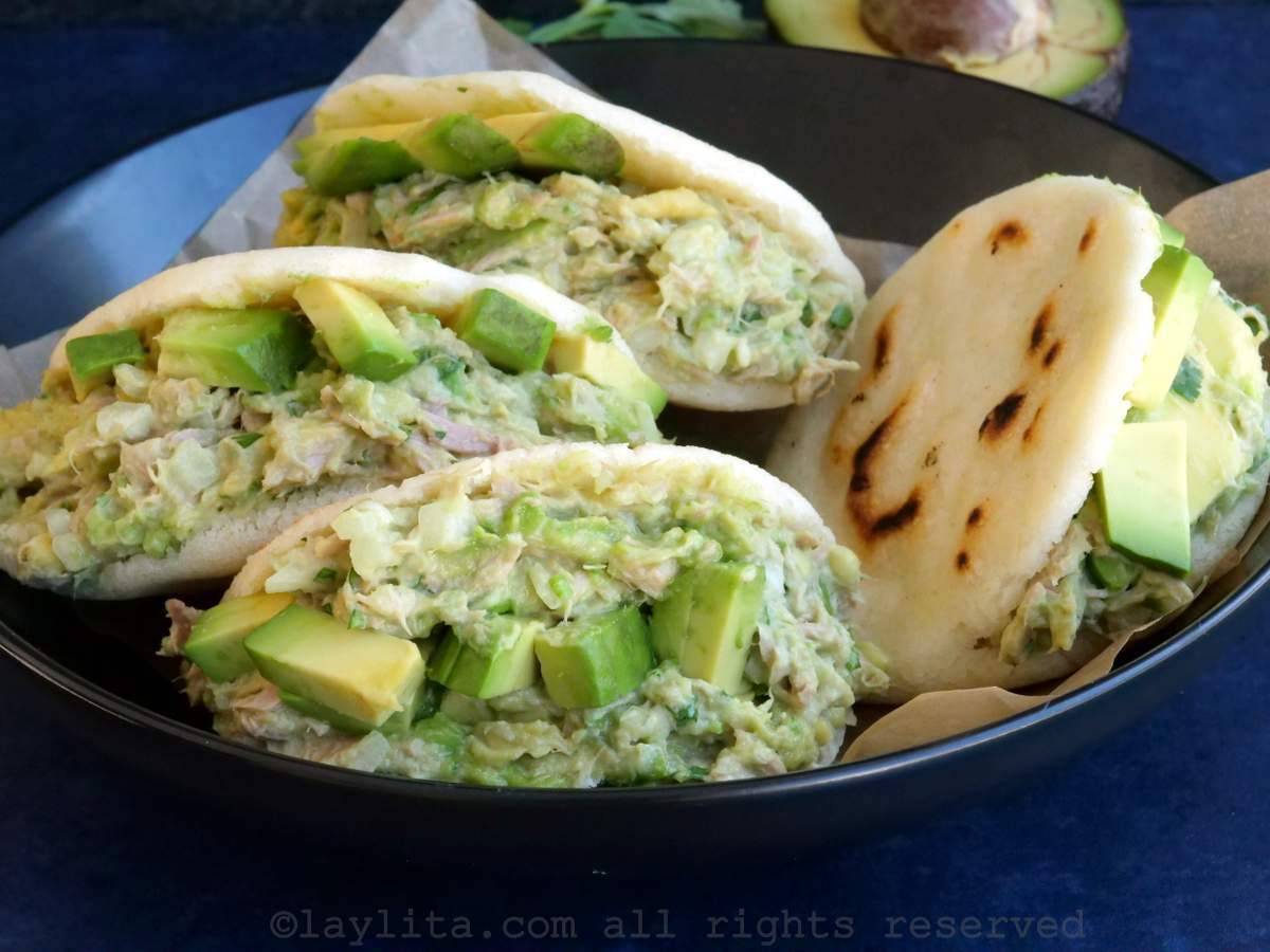 Four arepas filled with tuna avocado salad served in a bowl lined with parchment paper. 