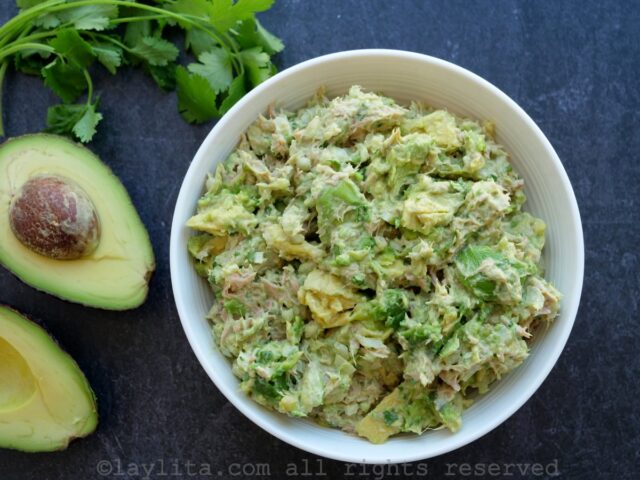 Avocado tuna salad in a bowl next to avocados and a sprig of cilantro