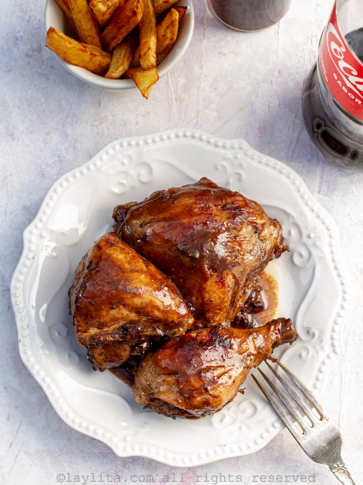 Overhead shot of pollo a la coca cola served on a white plate with fries on the side.