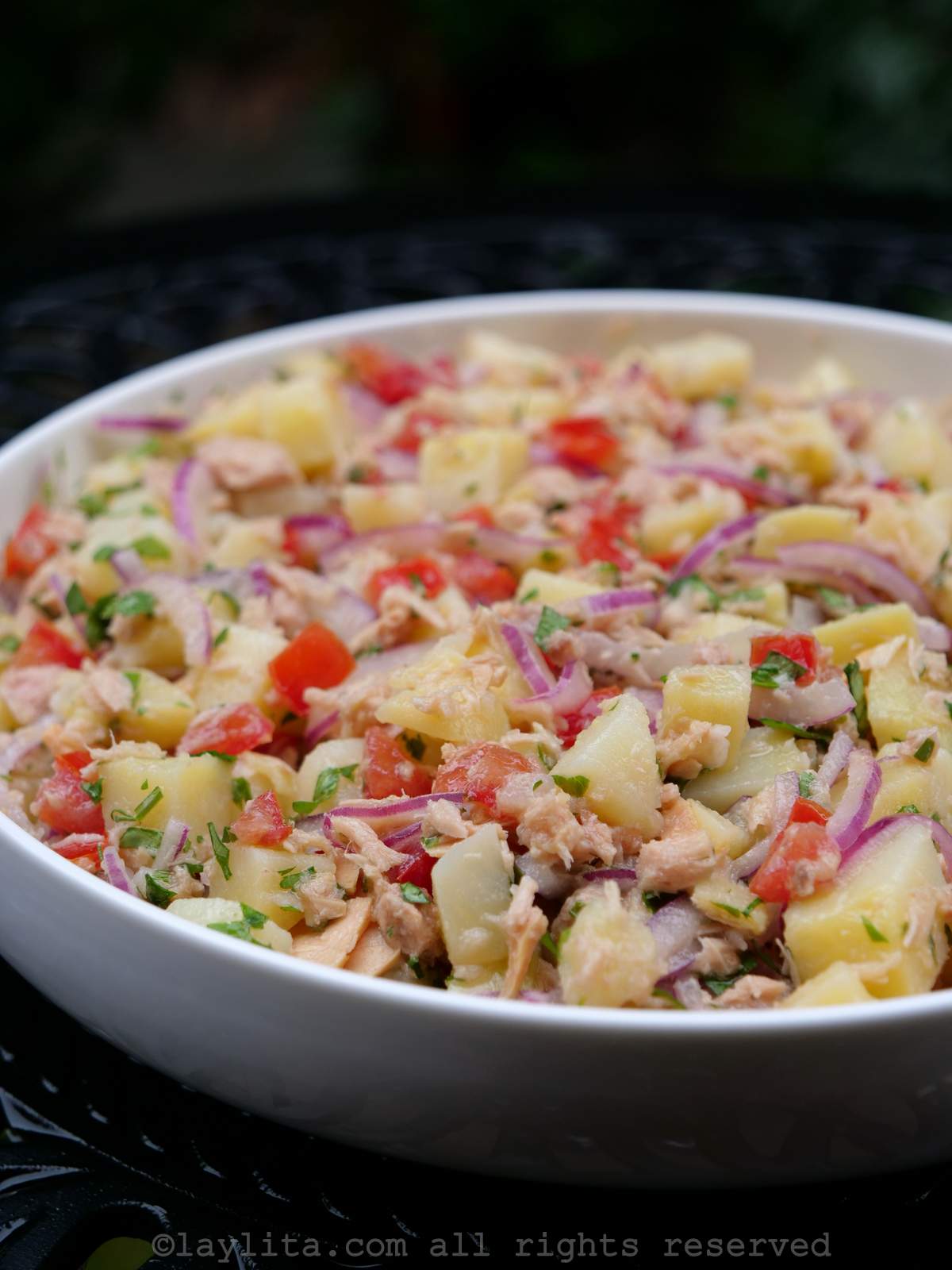 Side view of the tuna potato salad served in a shallow white dish with a black background