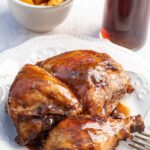 Close up shot of coca cola chicken on a white plate next to a class of soda in a coca cola cup.
