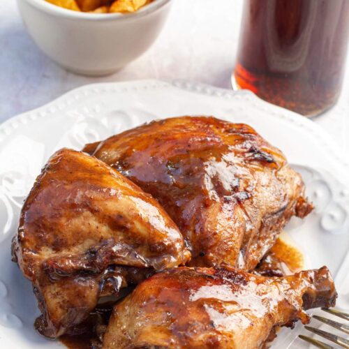 Close up shot of coca cola chicken on a white plate next to a class of soda in a coca cola cup.