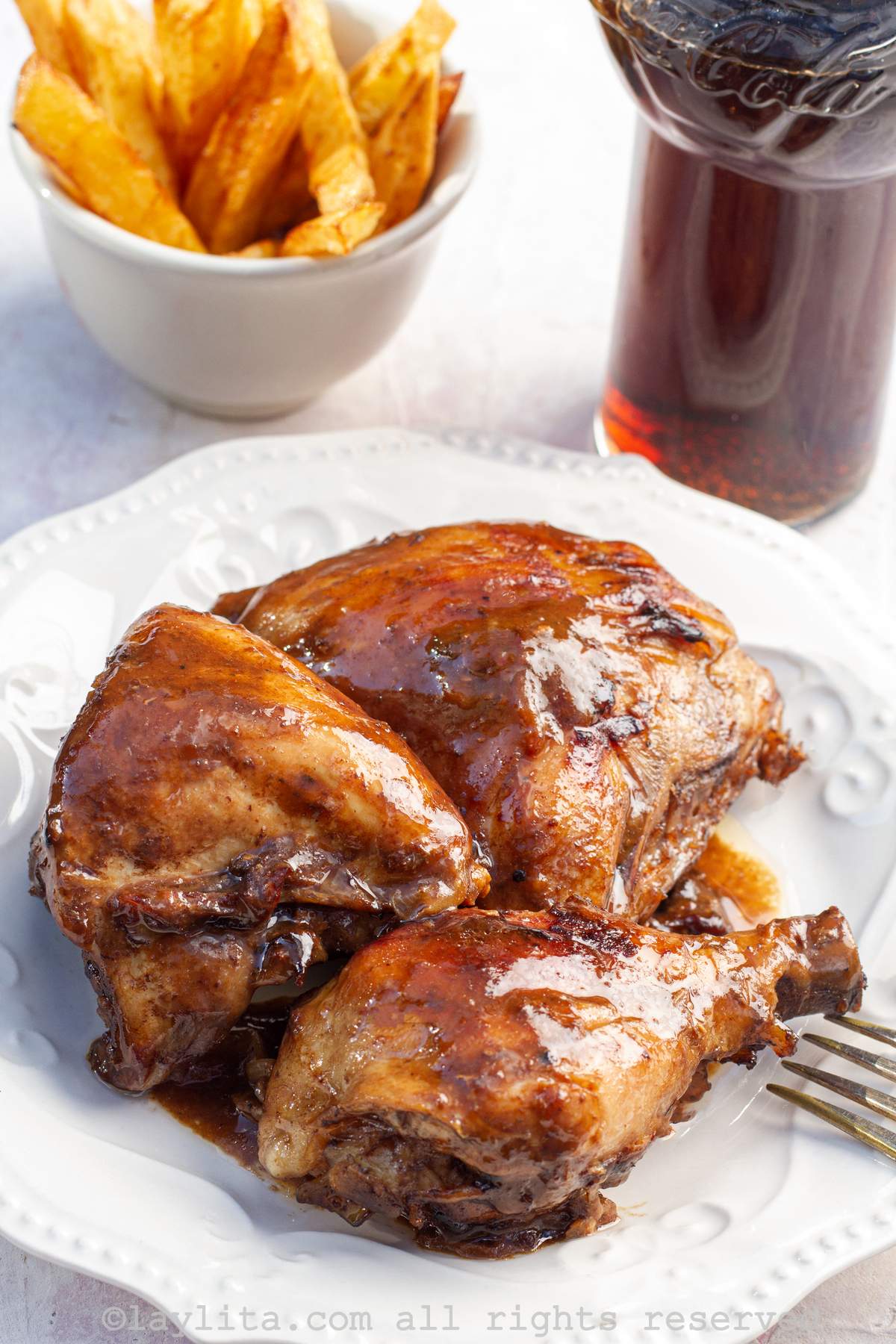Close up shot of coca cola chicken on a white plate next to a class of soda in a coca cola cup.