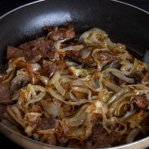 Liver and onions cooking in a large skillet