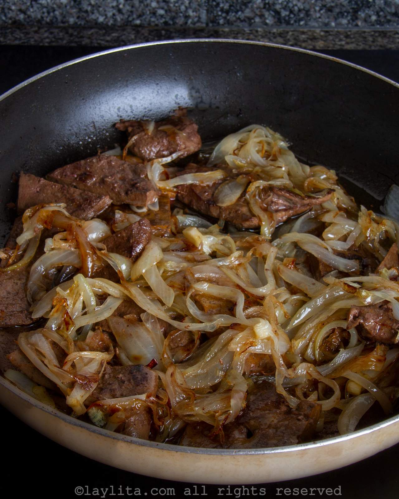 Liver and onions cooking in a large skillet