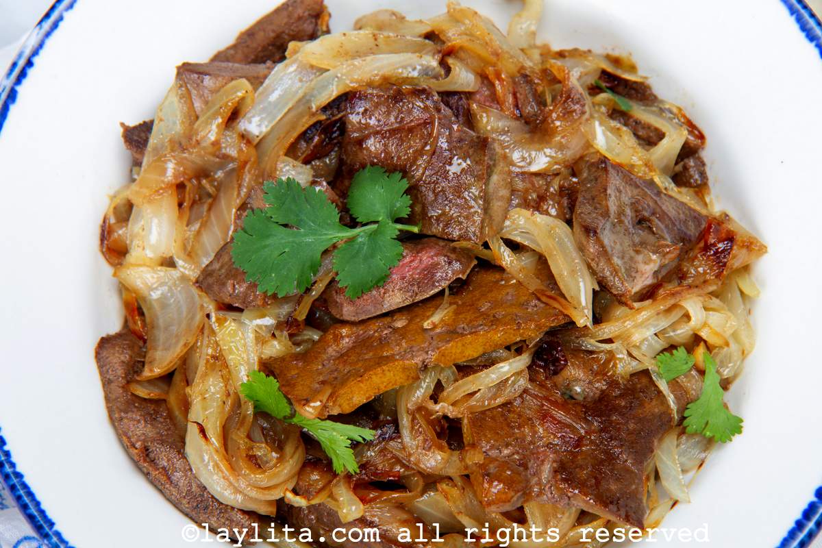 Close up of sauteed sliced beef liver and onions in a white and blue bowl garnished with cilantro