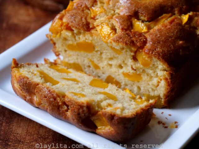 Side view of mango loaf cake on a white plate with one slice off the end to show the inside.