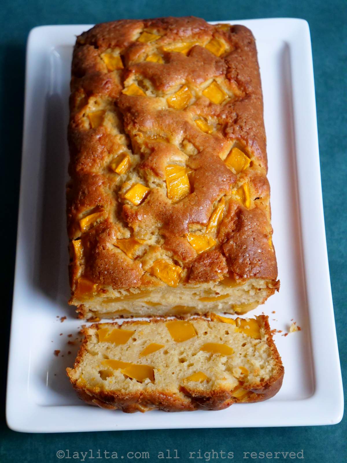 Overhead shot of mango loaf cake on a white plate with one slice off the end