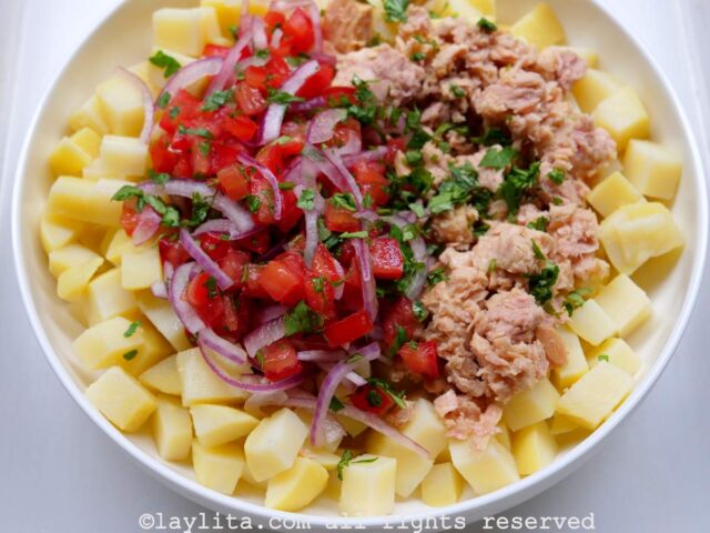 Potato tuna salad in a bowl with the tuna mixture on top of the bed of tomatoes in a white dish.