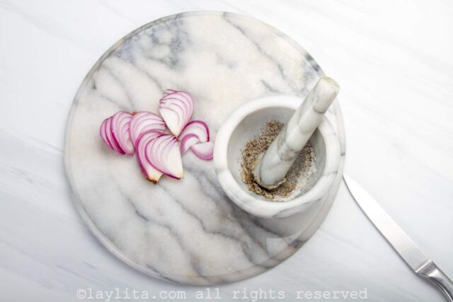Garlic being mashed in mortar next to sliced red onions