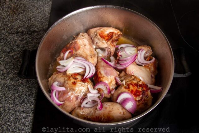 Chicken pieces with red onions added in a pan