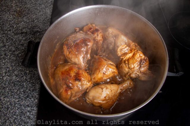 Pan on the stove full of chicken pieces cooked in coca cola sauce