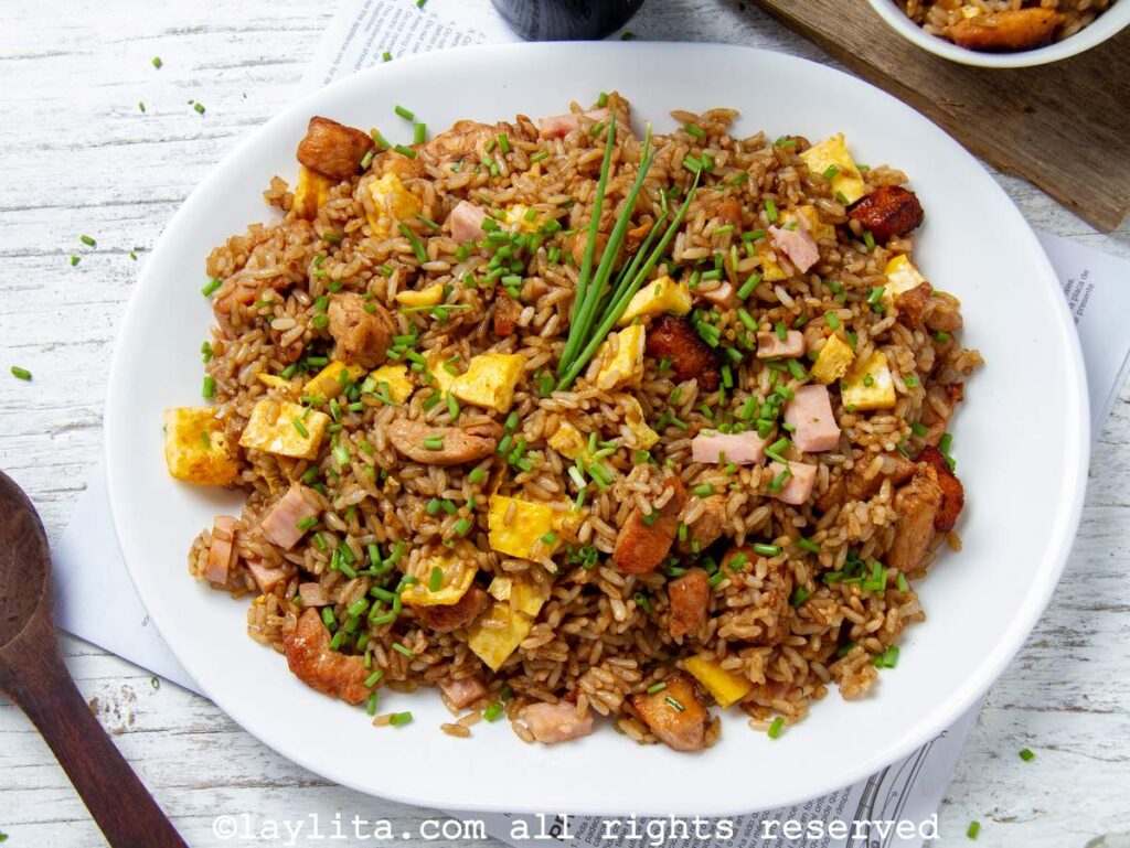 Overhead shot of arroz chaufa served on a white platter on a white wooden background next to a dark wooden spoon. 