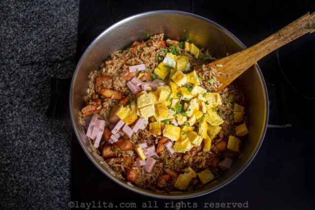 Adding the cooked chicken, ham and diced omelet to the pan with the rice