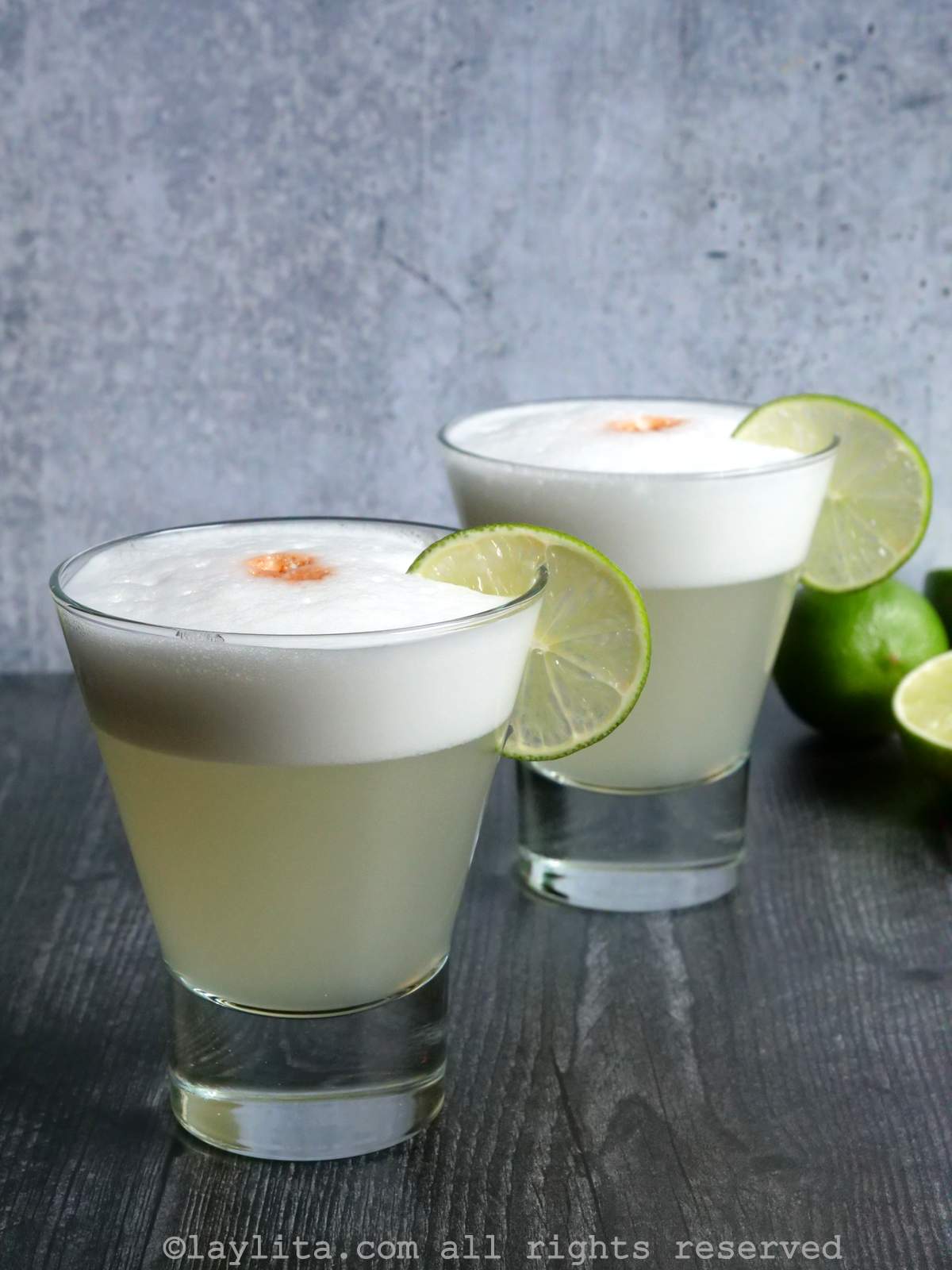 Side view of two pisco sours in tumbler glasses garnished with limes.
