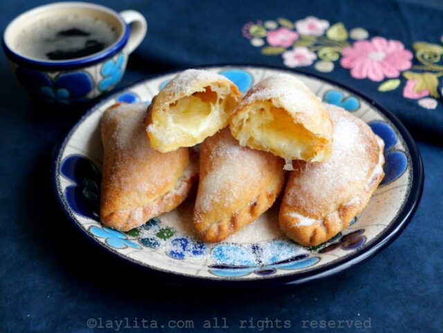 Air fryer cheese empanadas on a blue floral plate with one on top cut in half.