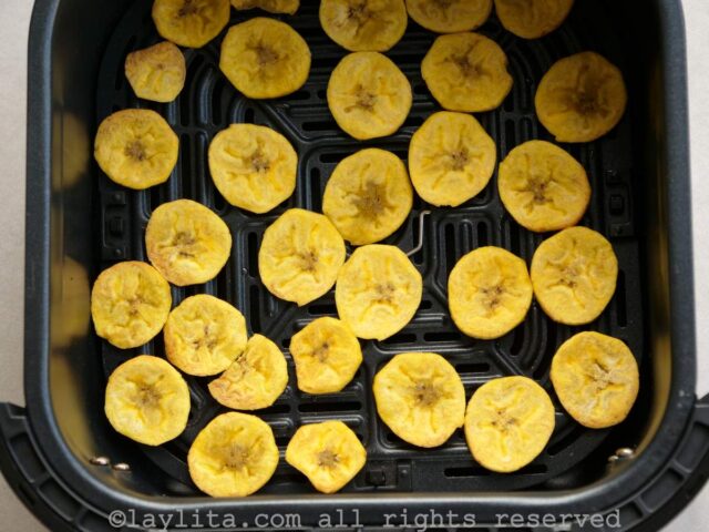 Sliced green plantains cooking in the air fryer basket.