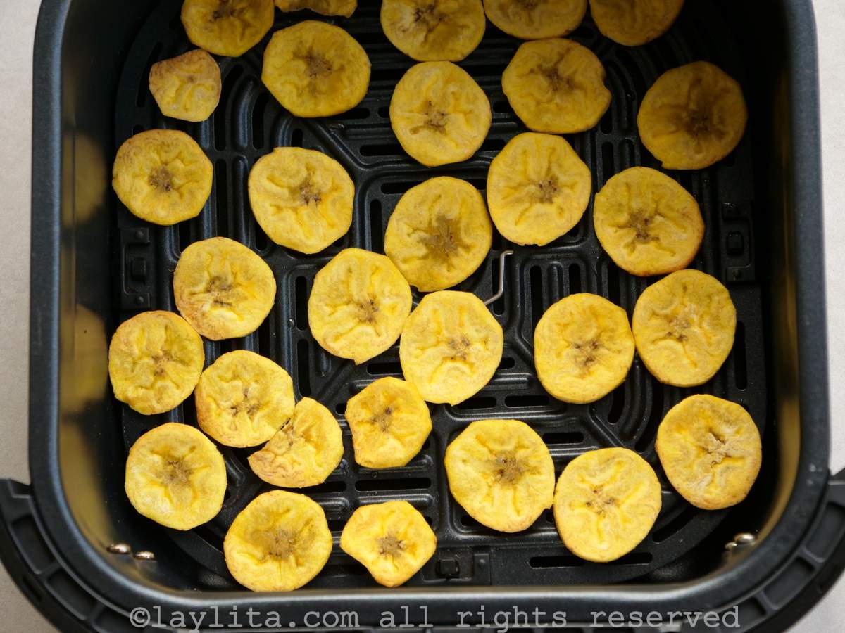 Sliced green plantains cooking in the air fryer basket.