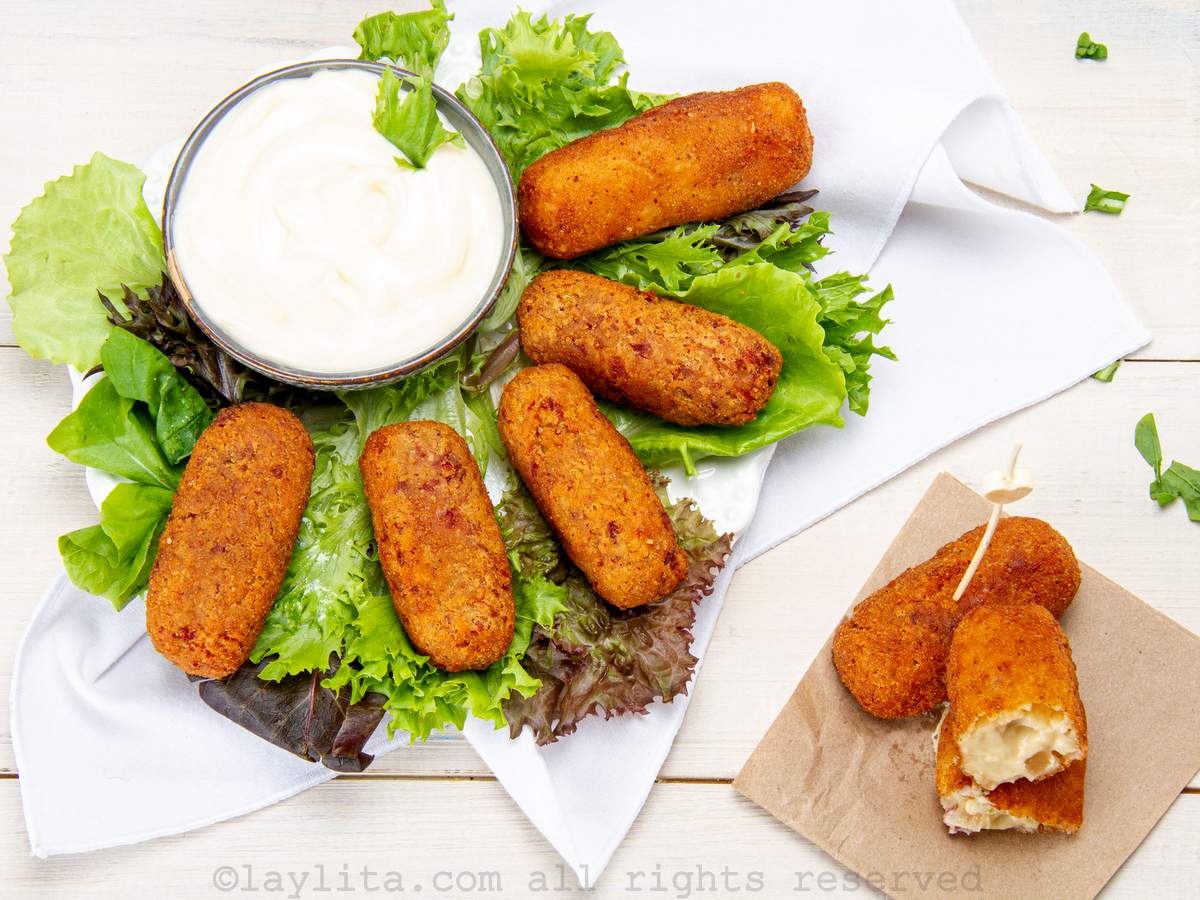 Overhead shot of Spanish croquettes served on a bed of lettuce with a dipping sauce with two croquettes on a napkin on the side.