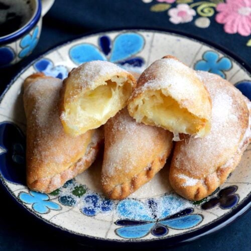 Overhead shot of air fryer cheese empanadas on a blue floral plate with one on top cut in half.