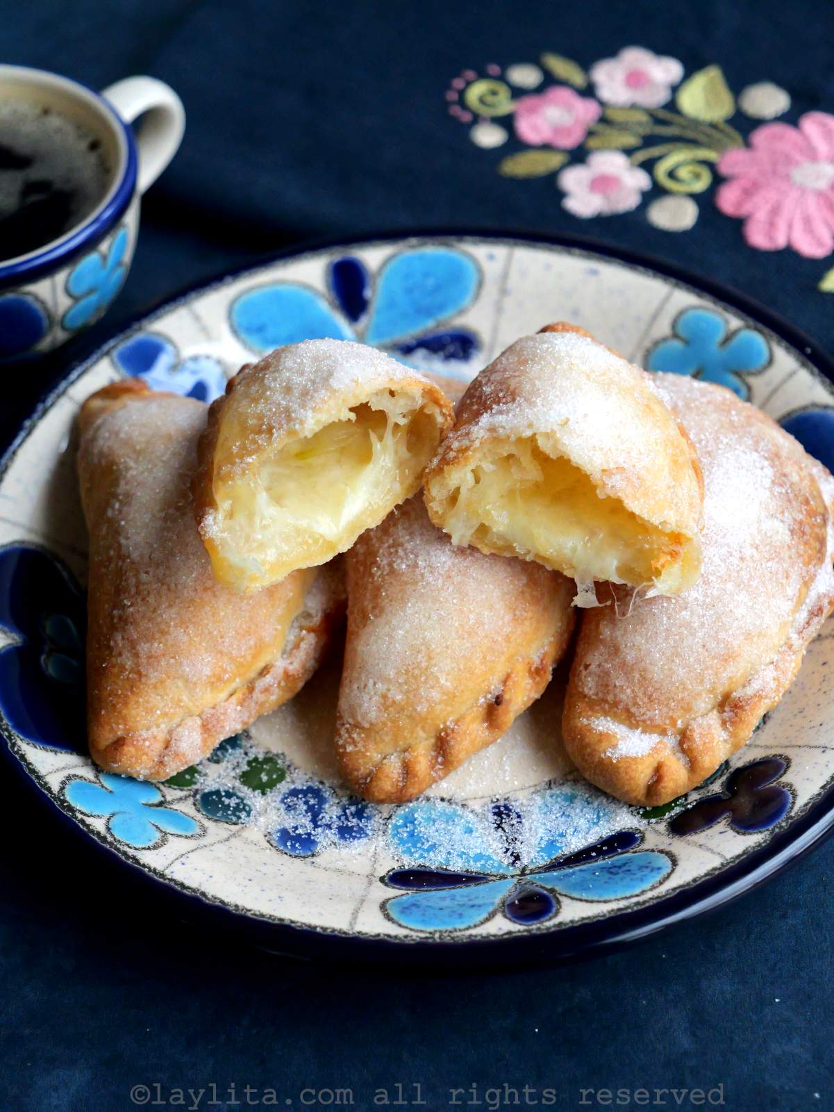 Overhead shot of air fryer cheese empanadas on a blue floral plate with one on top cut in half.