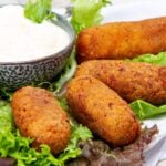 Four croquettes served on a plate on a bed of lettuce served with a dipping sauce.