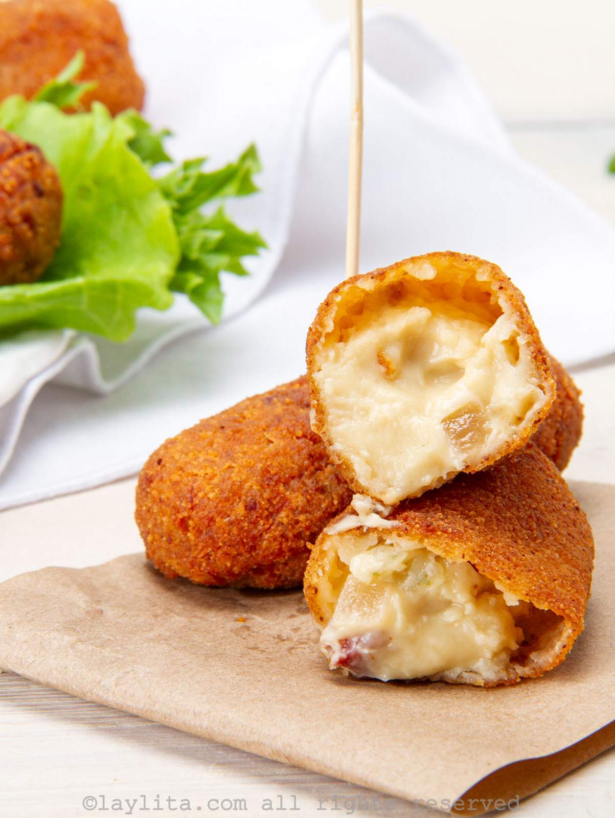 Two croquettes on a napkin with one broken in half to show the gooey inside.