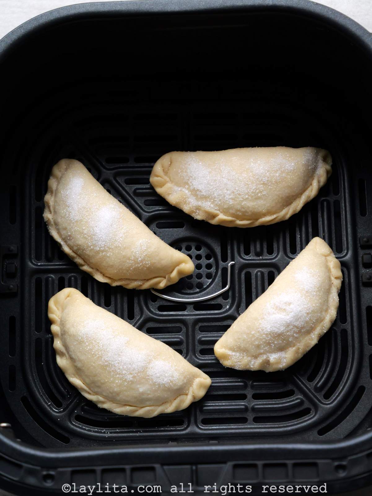 Overhead view of four uncooked empanadas in the air fryer