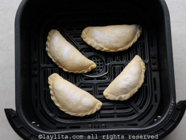 Air fryer cheese empanadas in the air fryer basket before cooking.