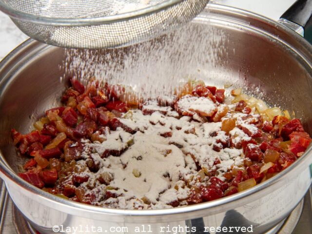 Adding flour to the ham and onion mix in a pan